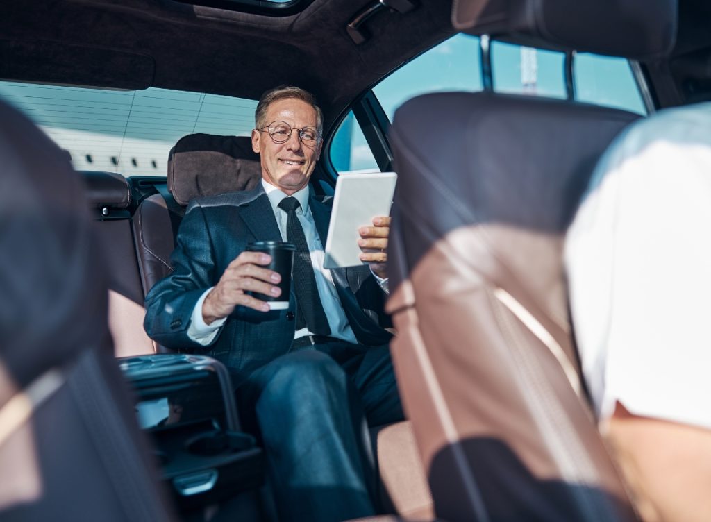 Uh businessman en train de travailler sur sa tablette à l'arrière d'une voiture haut de gamme conduite par un chauffeur privé.